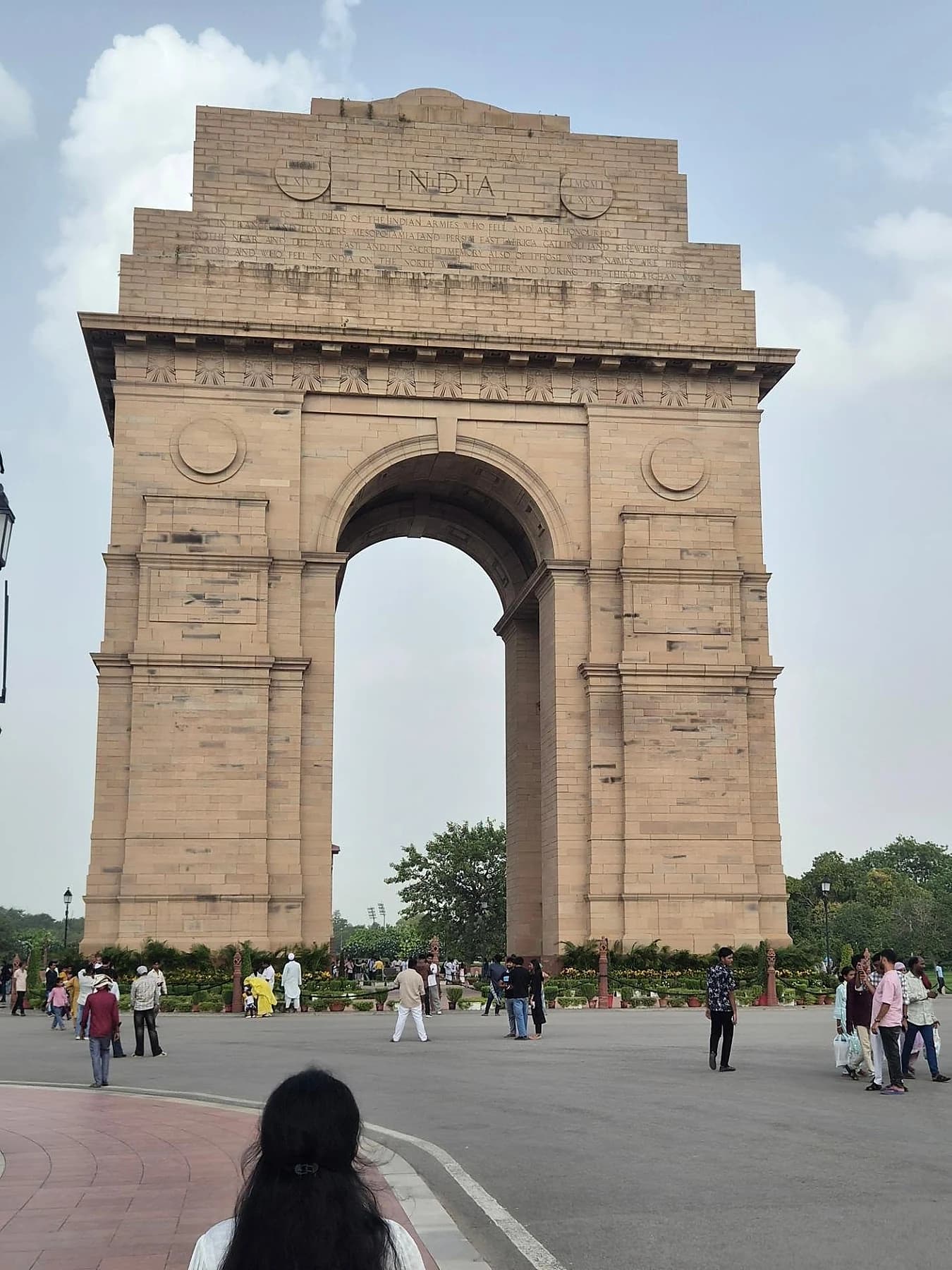 India Gate in New Delhi beneath a pale blue sky, with visitors crossing the plaza