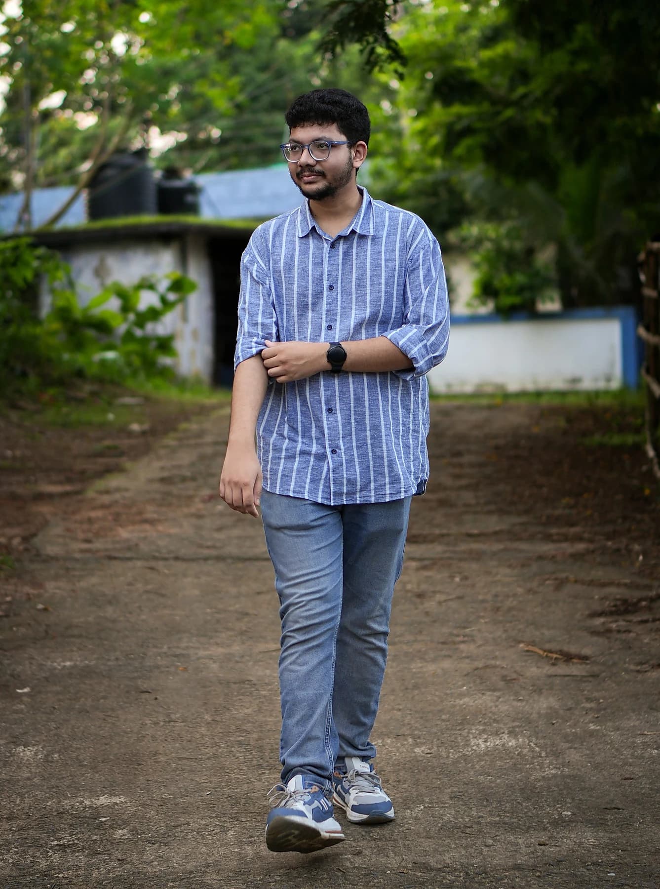 Raktim Ranjit in a blue striped shirt standing on a shaded garden path