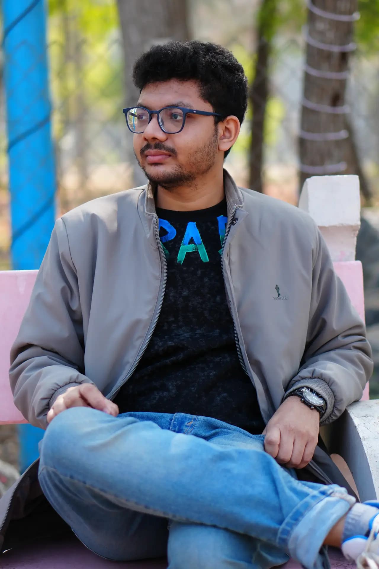 Raktim Ranjit in a grey jacket looking away from the camera, sitting against a blue and pink background