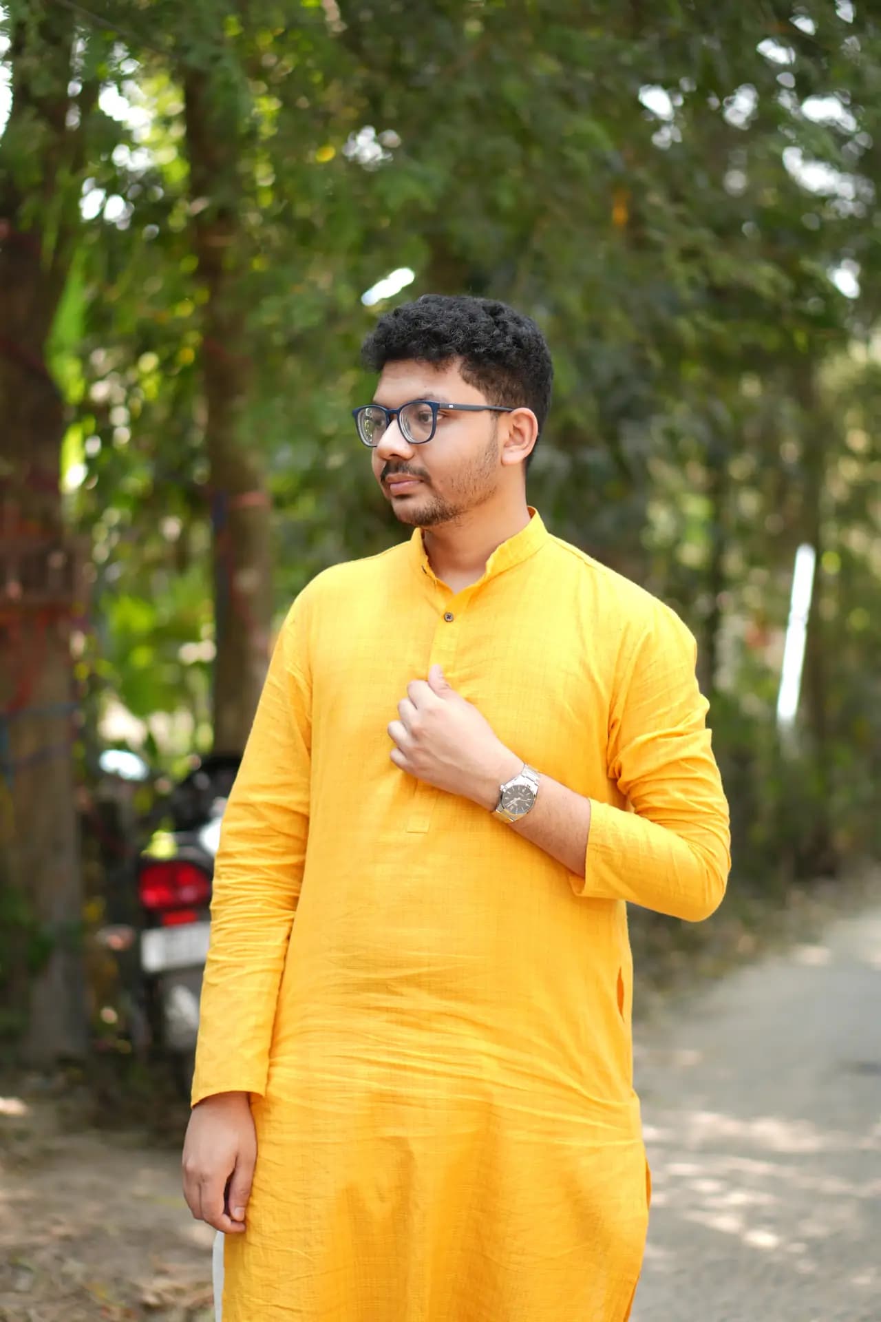 Raktim Ranjit in a yellow kurta, standing among trees with one hand on his chest