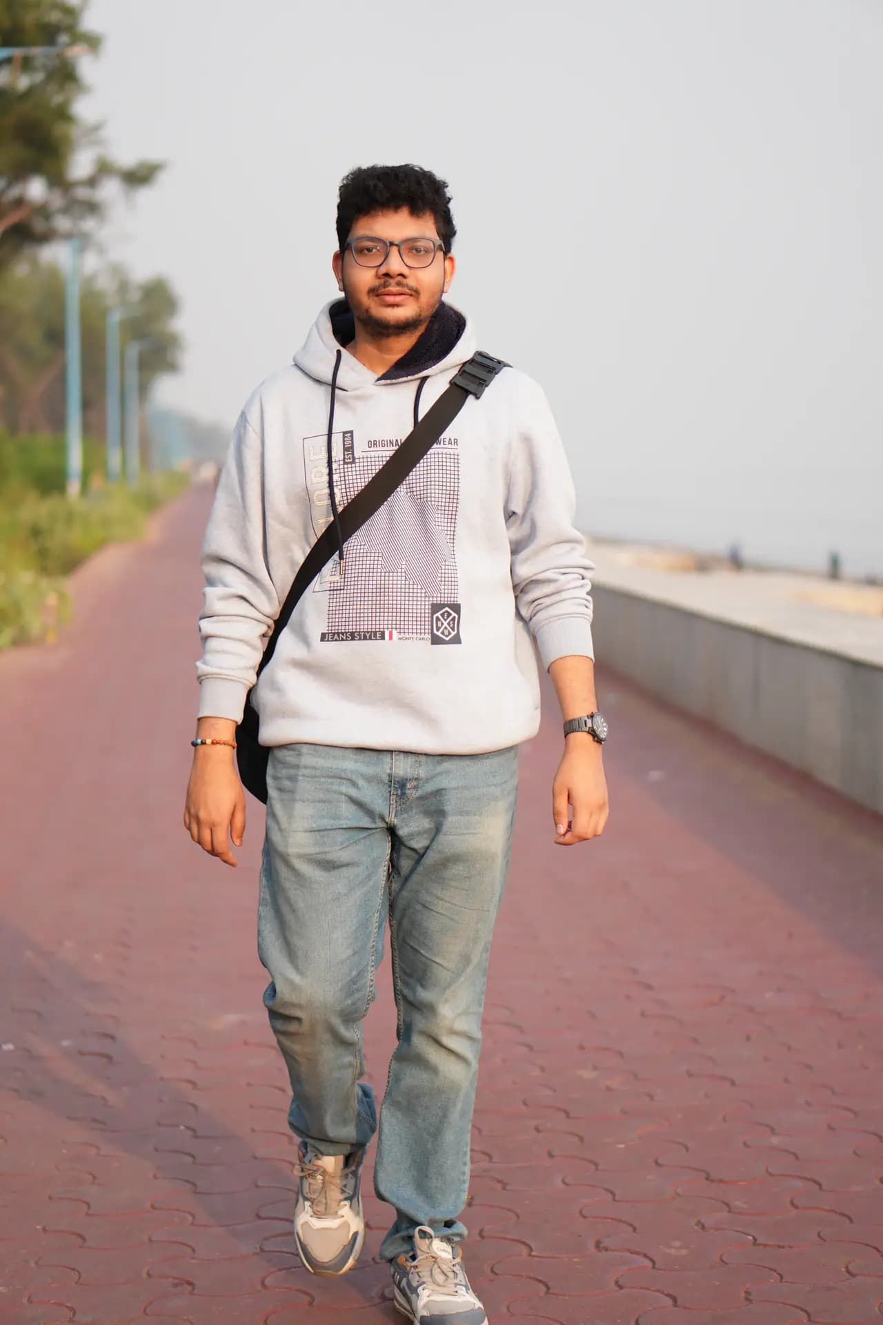Raktim Ranjit walking along a red brick path next to a seafront wall